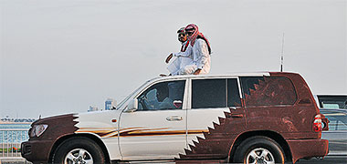 Two Qataris sitting on the roof of their car on National Day
